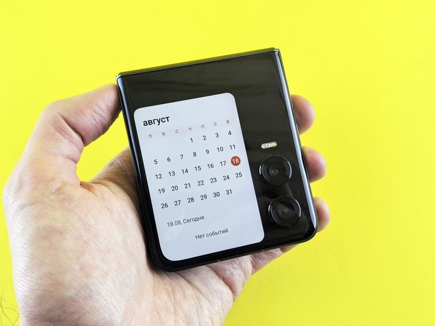 Person holding a compact clamshell flip phone displaying widget screen