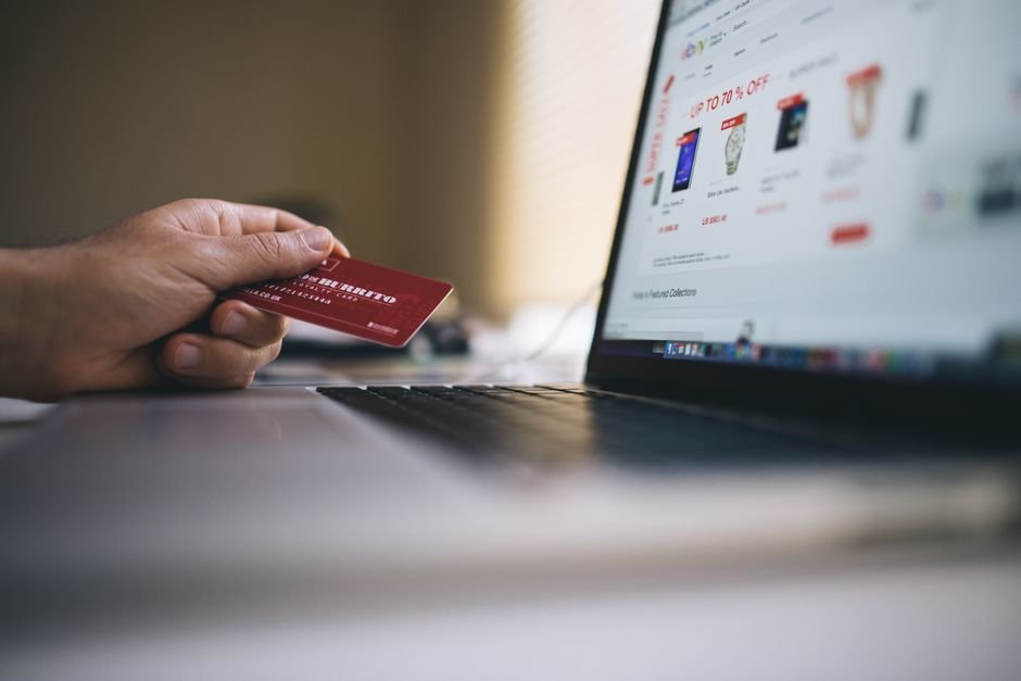 Shopper holding credit card while analyzing electronic discounts and festival sales on laptop