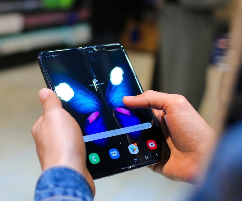 Hands opening a modern book-style foldable smartphone showing interior flexible screen