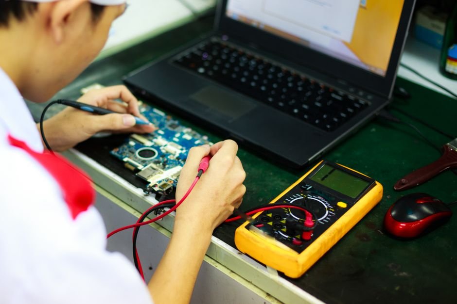 Technician running electrical multimeter diagnostic on aging laptop motherboard
