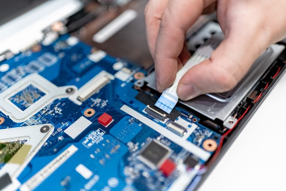 Hands examining laptop circuit board with technician tools indicating hardware aging