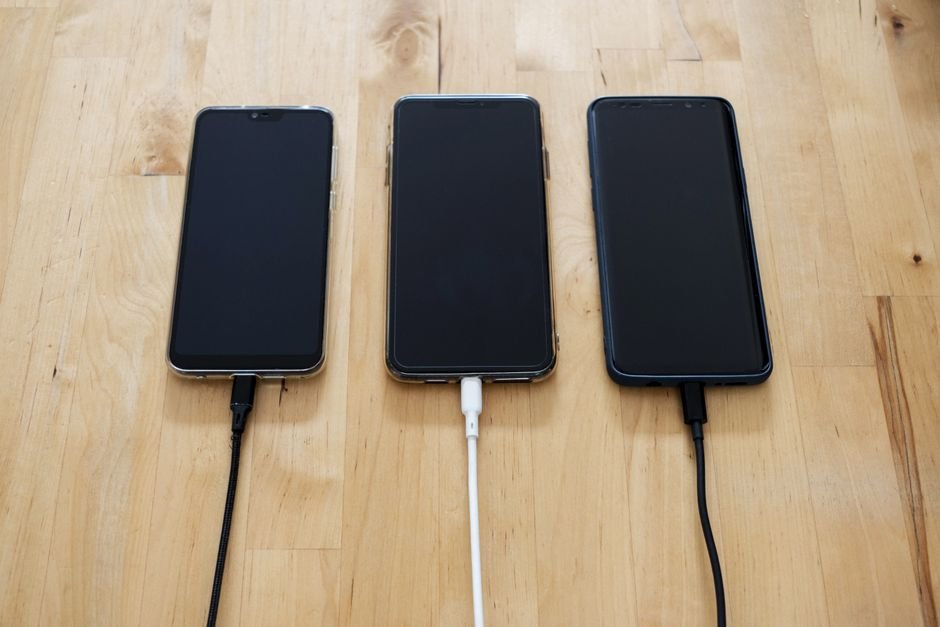 Multiple smartphones plugged into charging adapters on a table surface
